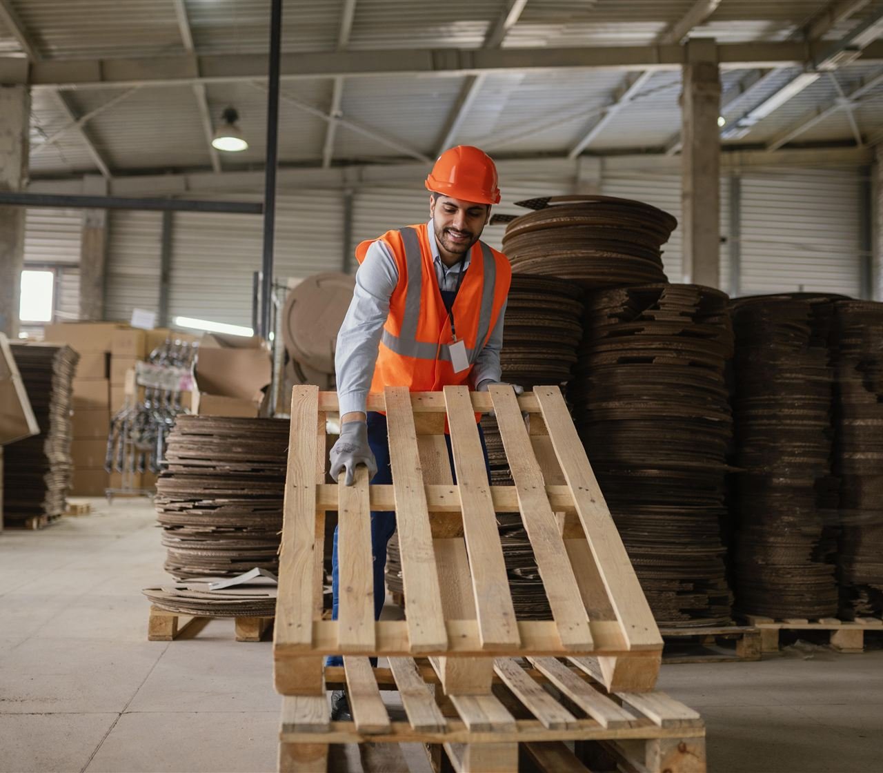 Trabalhador com equipamentos de proteção organizando pallets em galpão